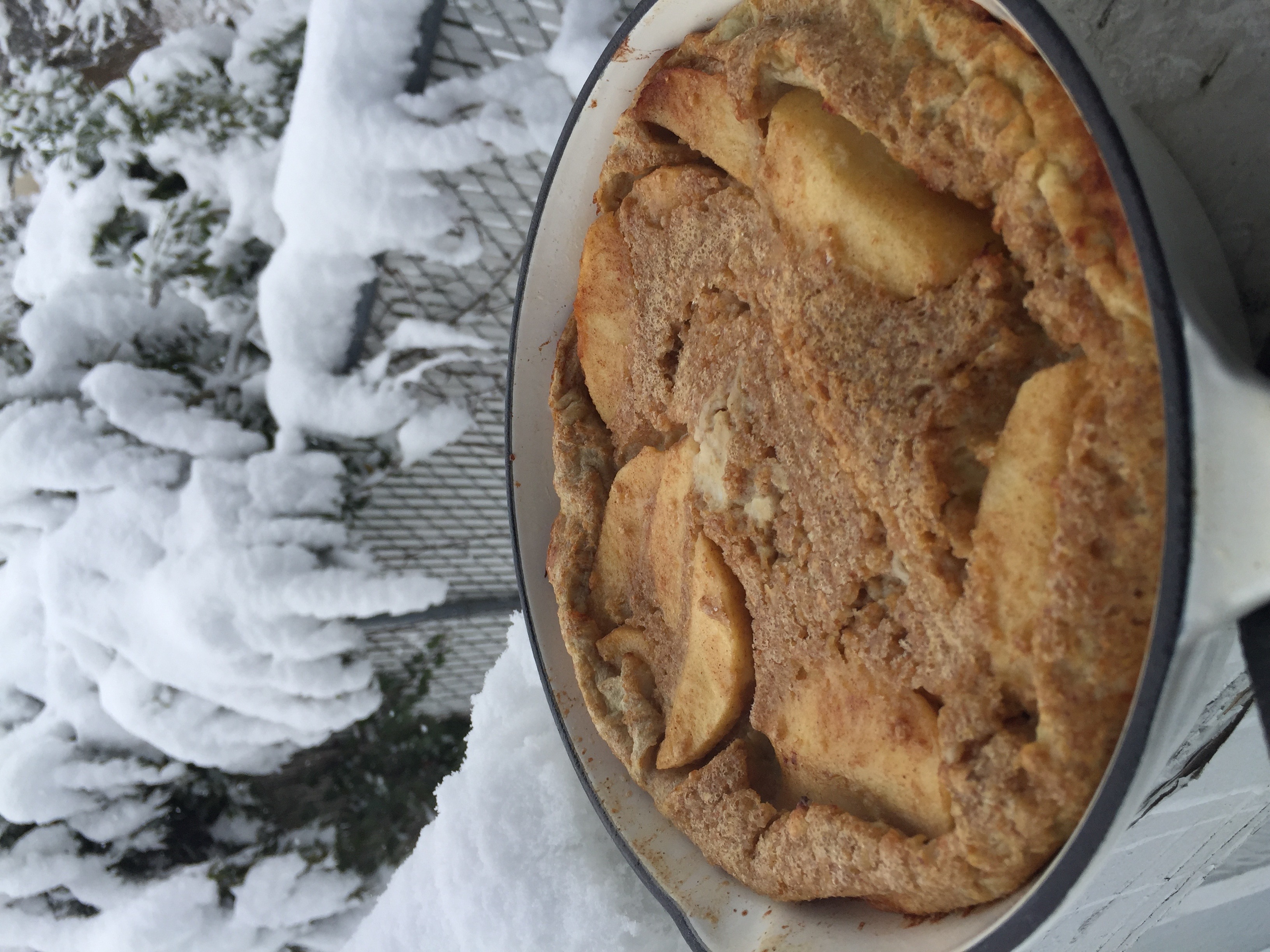 Cardamom apple Dutch baby, fresh from the oven, set against a snowy railing