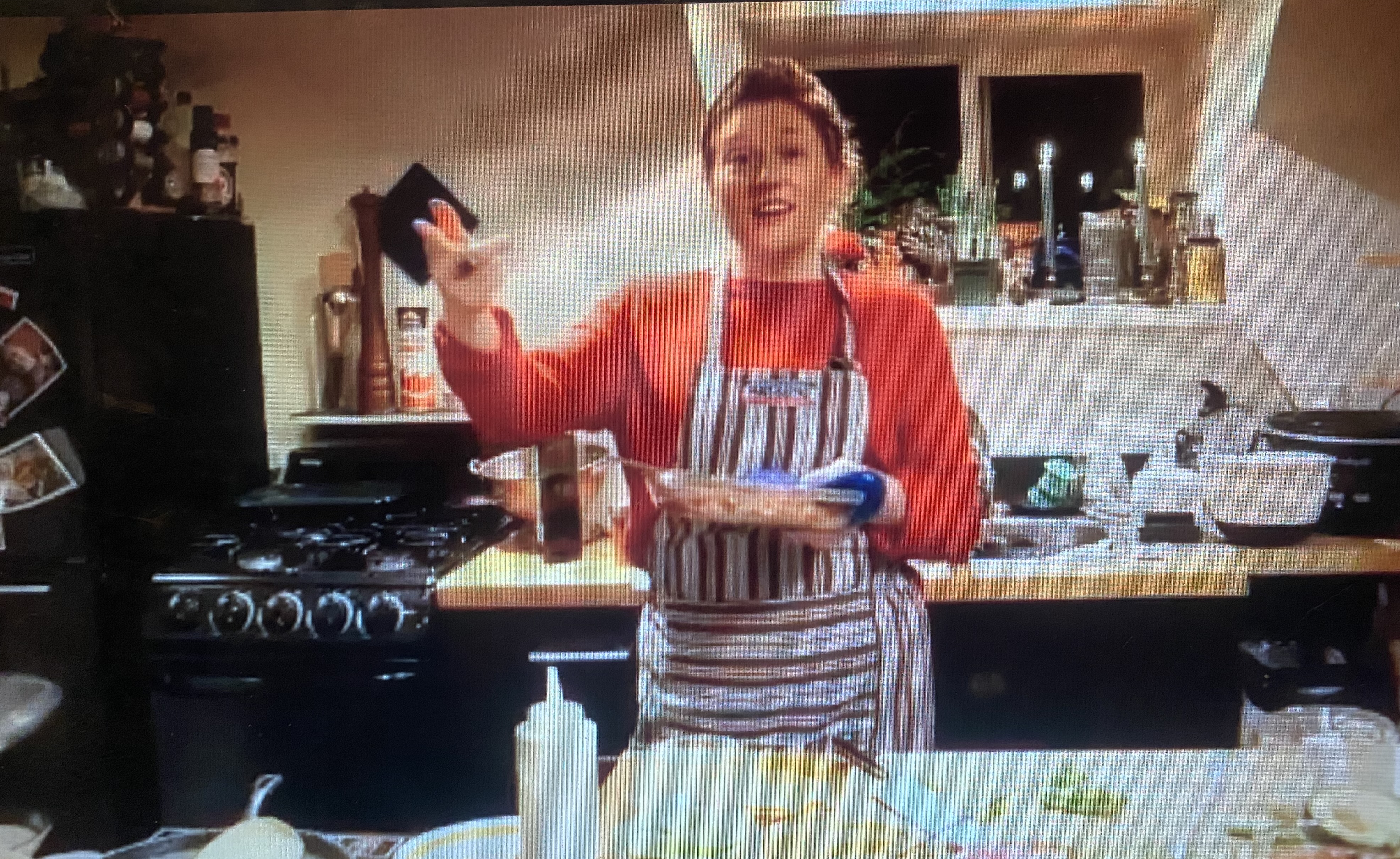 Emily mid-teaching in her kitchen, gesturing while holding a dish, during a cooking class