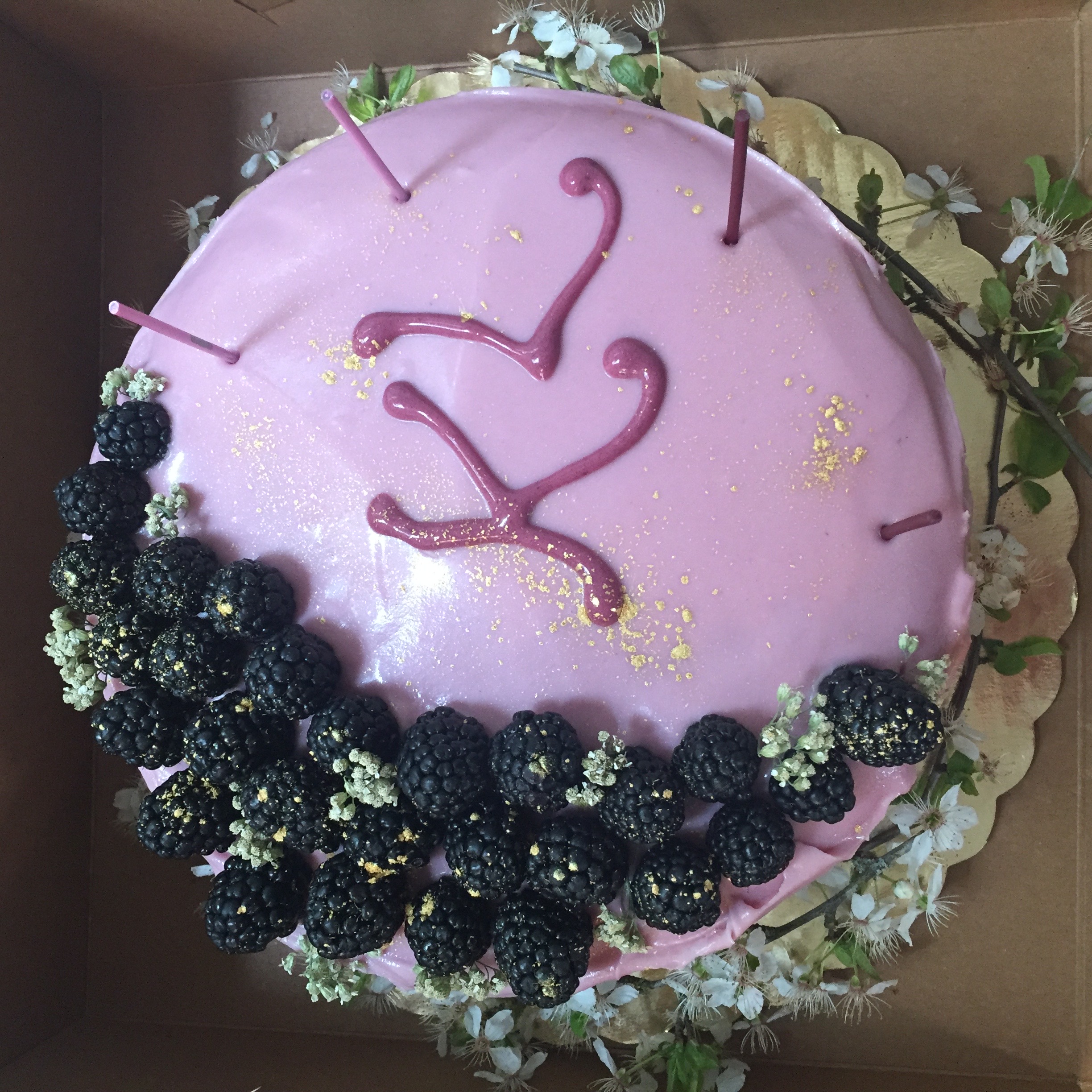 Custom birthday cake with pink glaze, fresh blackberries, and a piped monogram