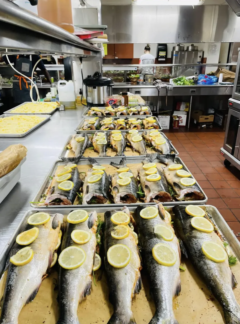 Rows of whole fish with lemon slices being prepped on sheet pans in a commercial kitchen